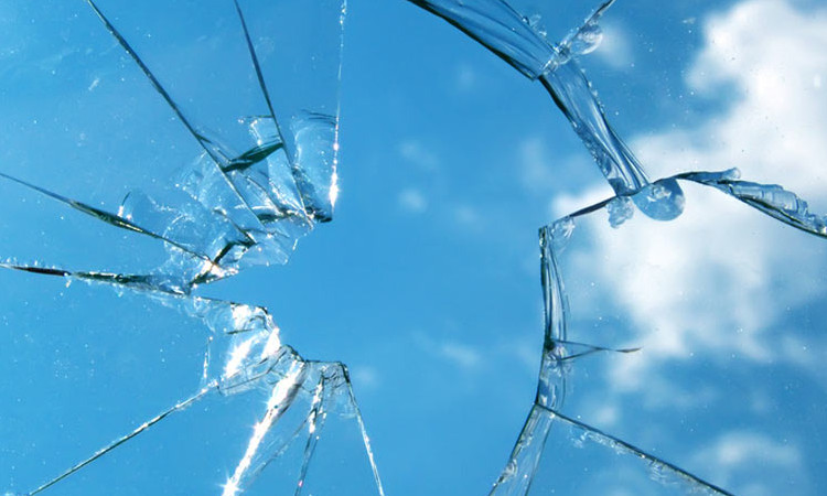 Zerbrochene Glasscheibe vor blauem Himmel mit kleinen Wolken.