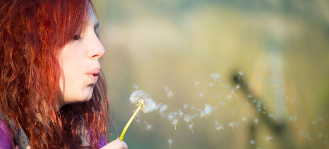 Jugendliches Mädchen pustet eine Pusteblume.