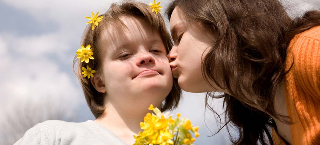 Ein Mädchen küsst ein anderes Mädchen mit Down-Syndrom auf die Wange.