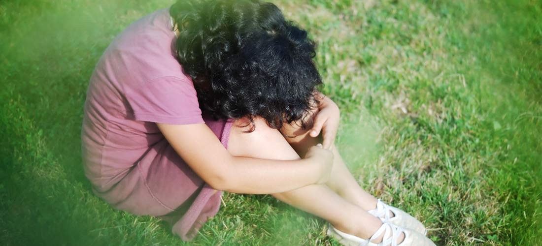 Jugendliche sitzt den Kopf auf Knie gebeugt auf Gras.