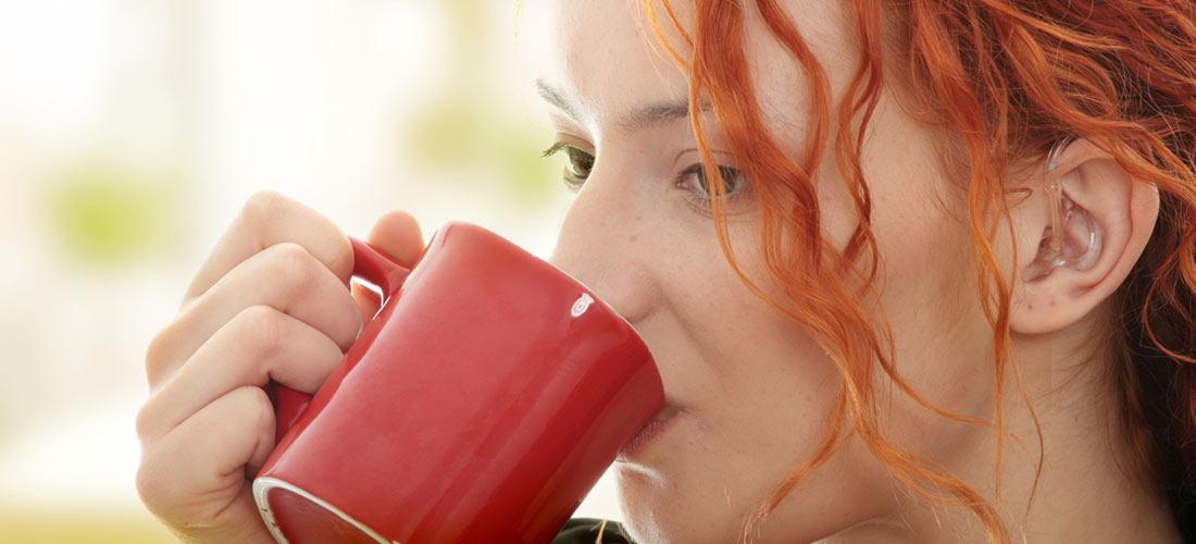 Mädchen trinkt aus einem Becher. Sie hat eine Hör-Hilfe im Ohr.