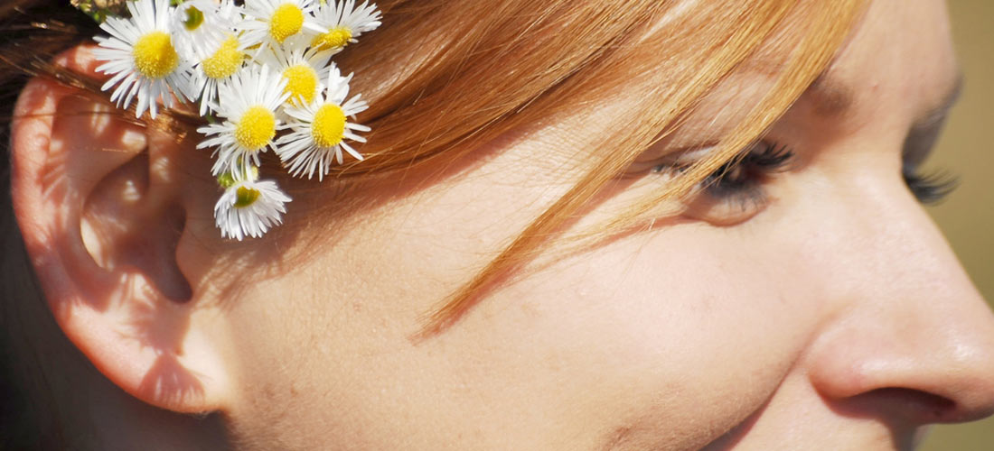 Mädchen aus seitlicher Sicht. Das Mädchen hat einen Blumen-Strauß mit Gänseblumen. Der Blumen-Strauß ist hinter ihrem Ohr.