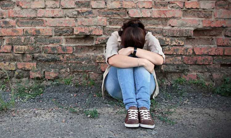 Mädchen sitzt vor einer Mauer. Die Mauer ist aus Ziegel-Steinen. Das Mädchen hat ihren Kopf auf die Knie gelegt. Mädchen sitzt vor einer Mauer. Die Mauer ist aus Ziegel-Steinen. Das Mädchen hat ihren Kopf auf die Knie gelegt.