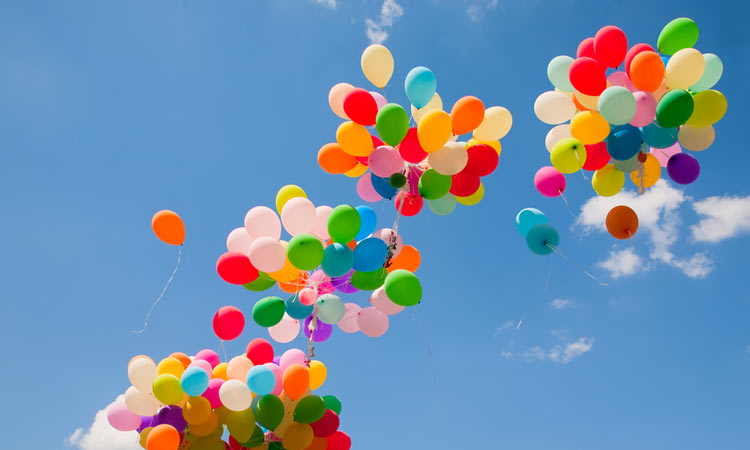 Bunte Luftballons fliegen in drei Gruppen in den blauen Himmel.