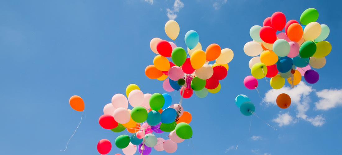 Bunte Luftballons fliegen in drei Gruppen in den blauen Himmel.