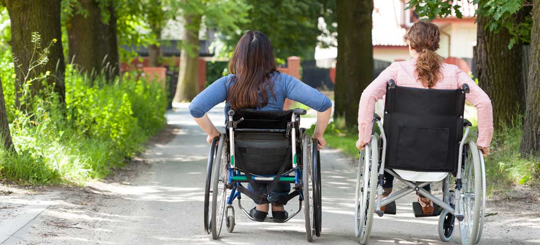 Zwei Rollifahrerinnen von hinten nebeneinander auf  einem Weg.